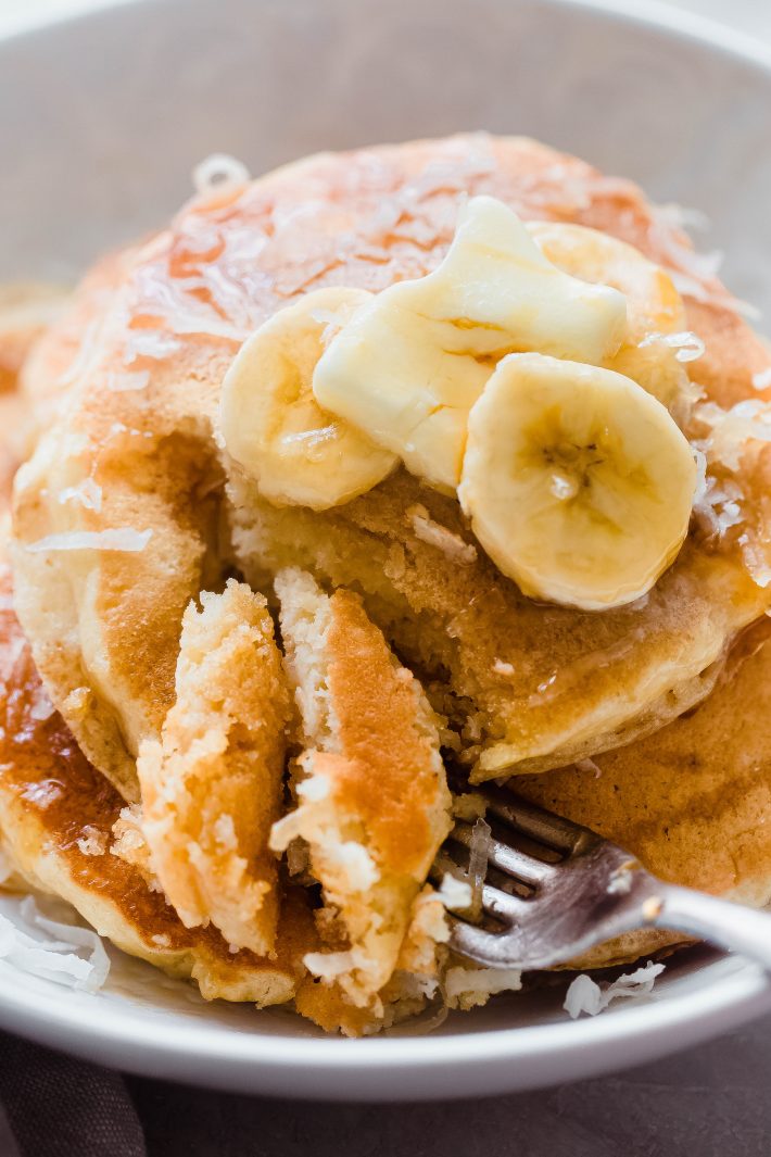 plate with pancakes topped with banana slice sand butter pat