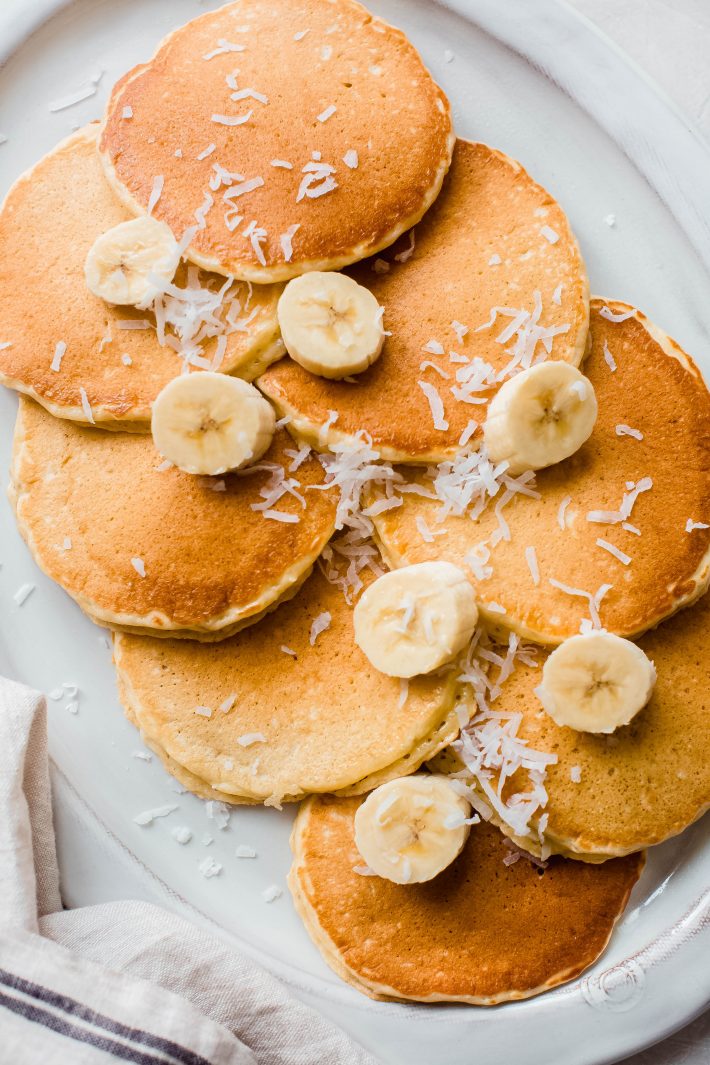 prepared coconut banana pancakes with banana slices and shredded coconut on platter
