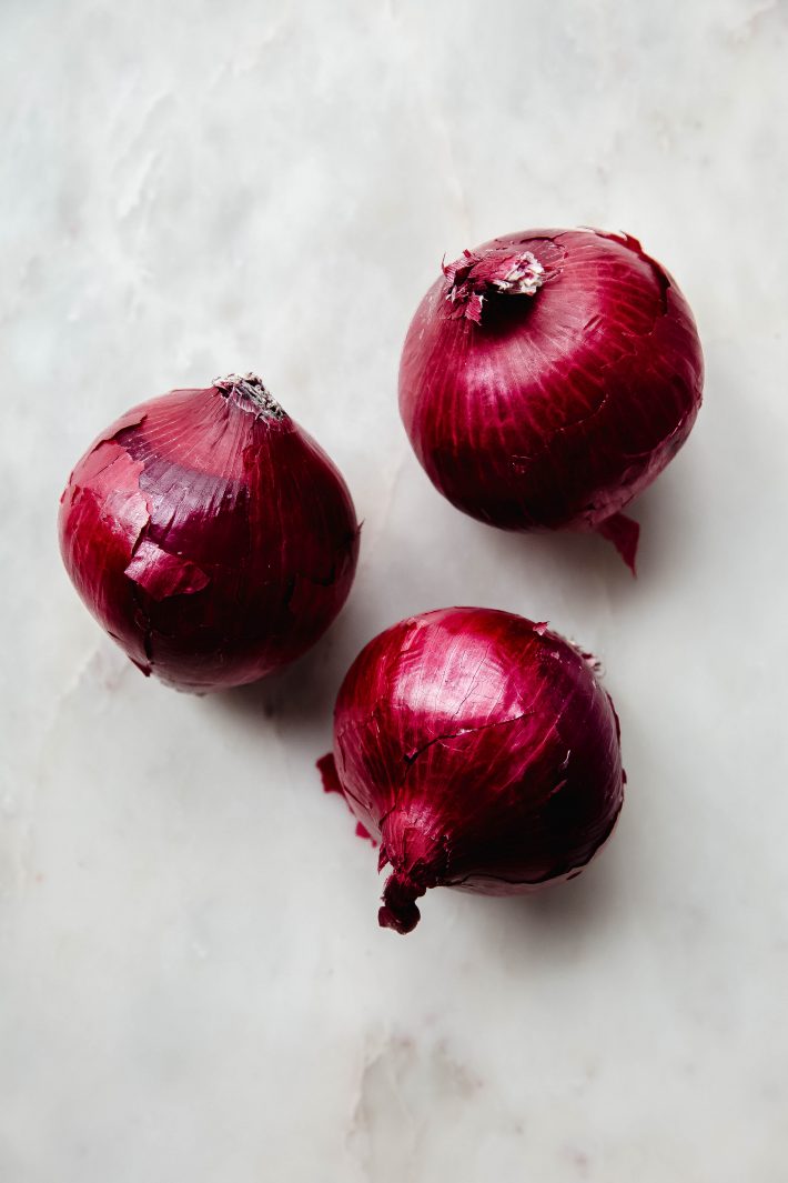 three red onions on white marble