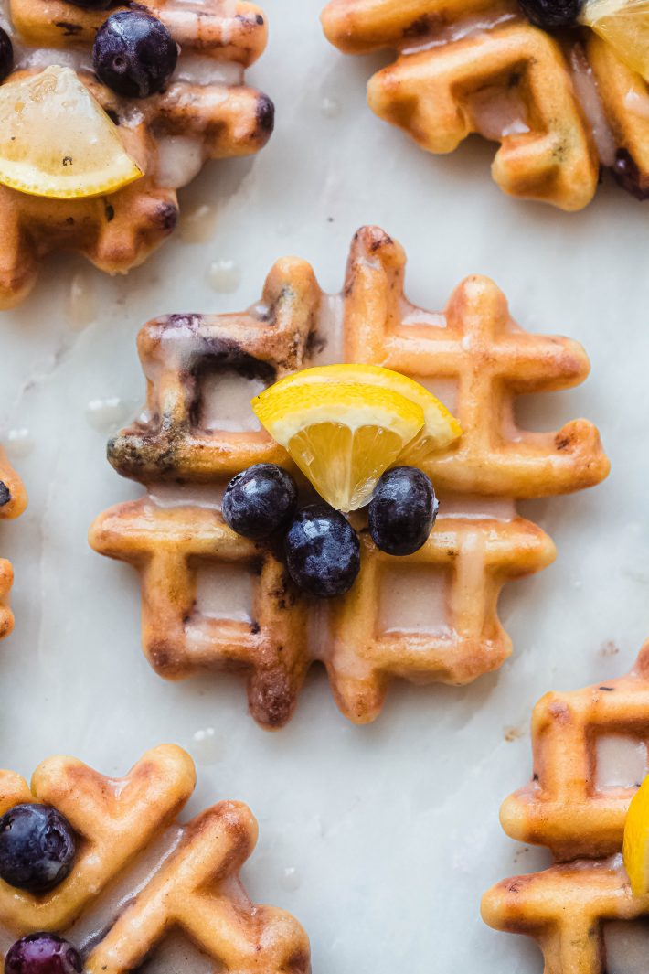 single glazed lemon blueberry waffle on white marble topped with lemon wedge and blueberries