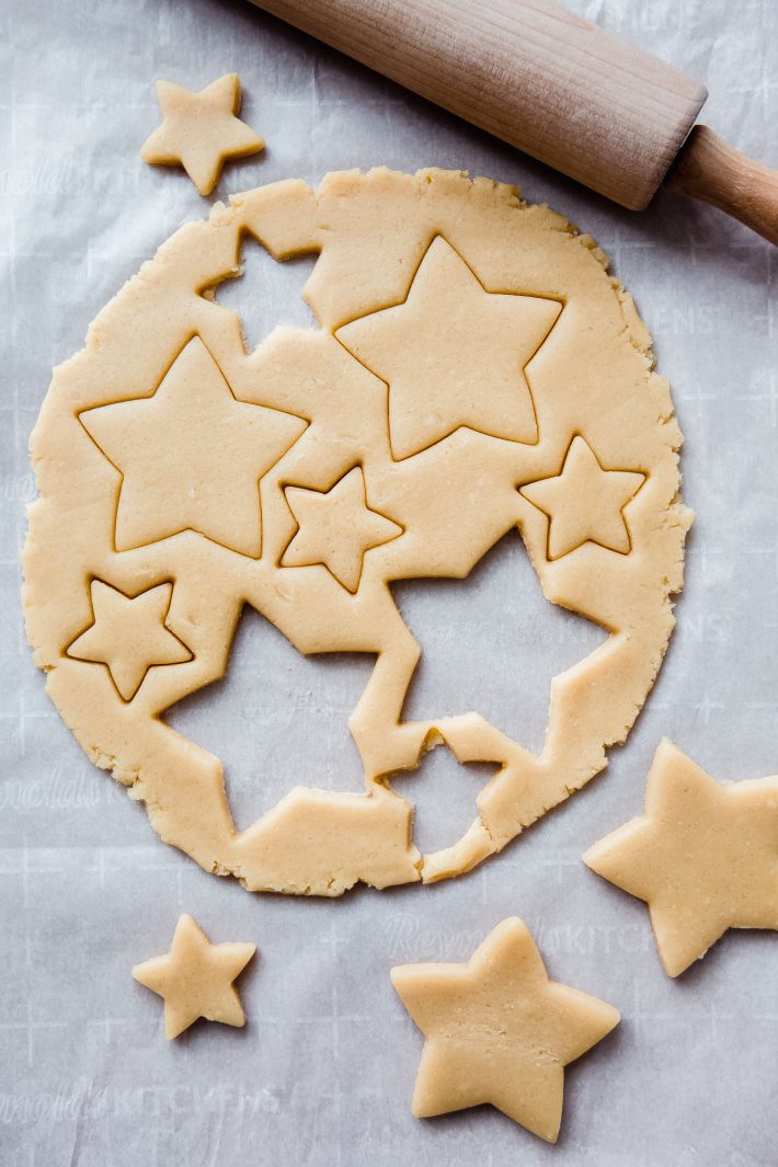 stars cut out of cookie dough with rolling pin on white parchment paper