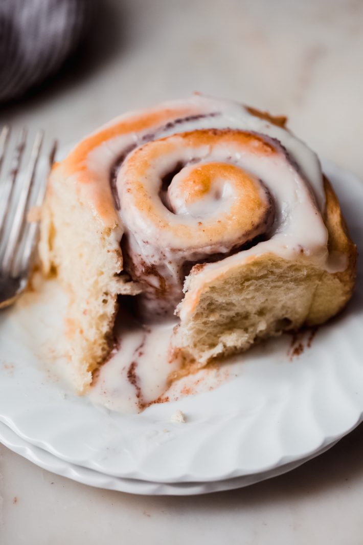 warm baked swirled cinnamon roll with icing on a white plate with fork