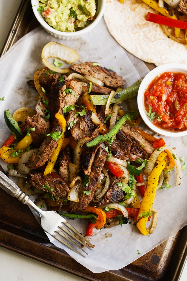 thinly sliced steak fajitas with colorful peppers and onions on sheet pan
