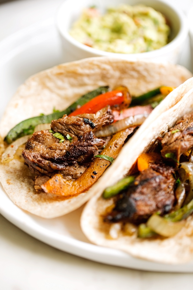 thinly sliced steak fajitas with colored peppers and onions on tortillas