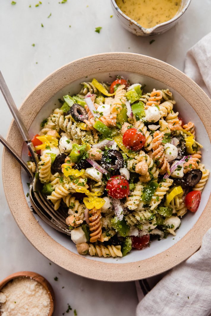 italian pasta salad in rimmed plate with fork and spoon on white marble