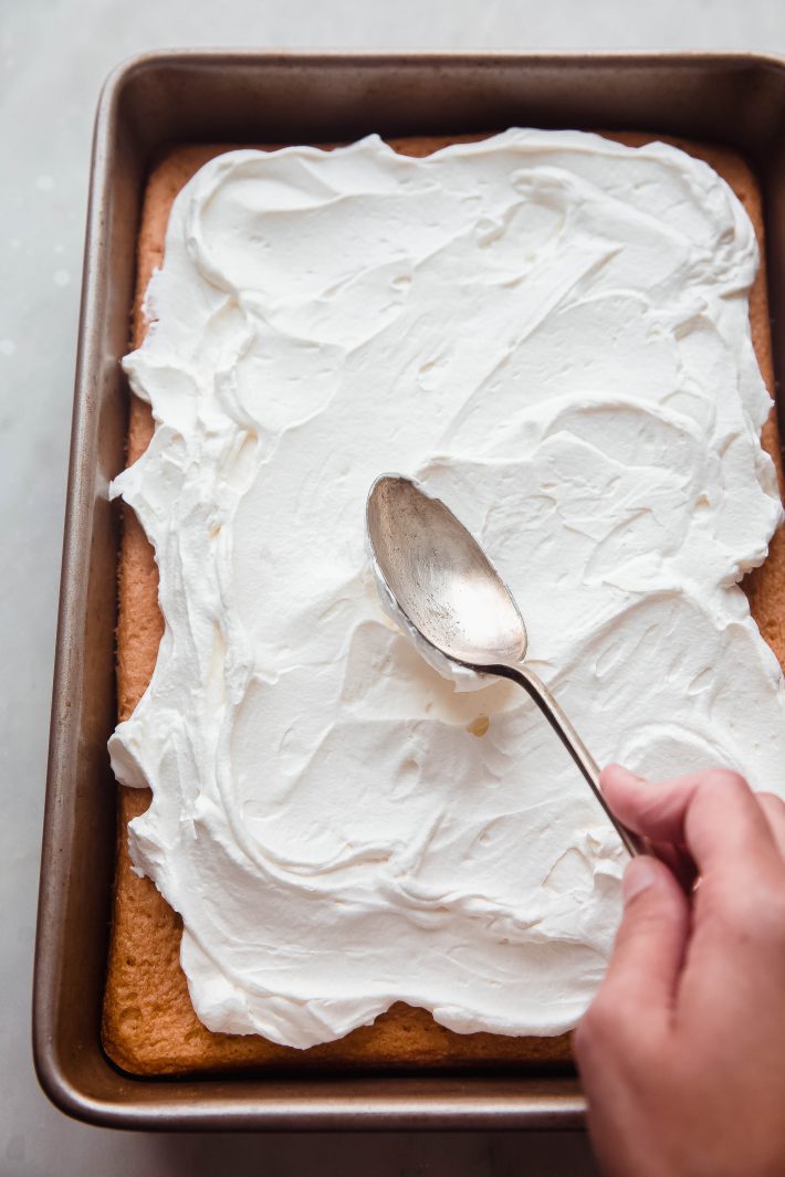 hand spreading whipped cream on cake with spoon