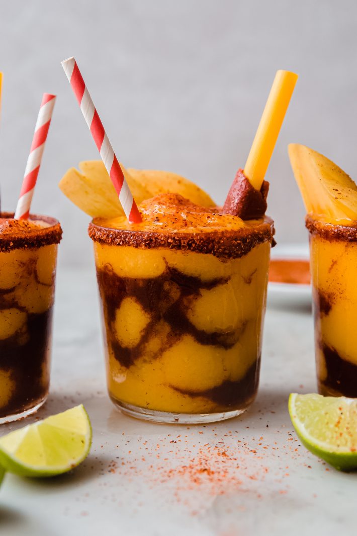 layered mangonada with lime wedges on white marble