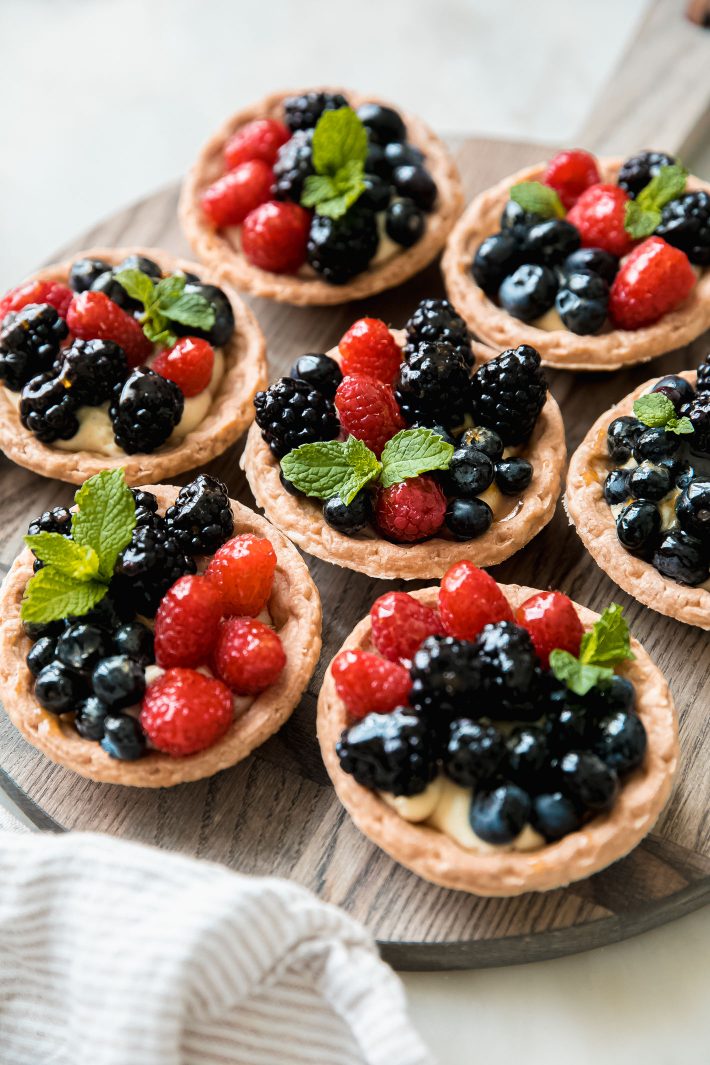 tarts on cutting board topped with fresh berries and mint sprigs