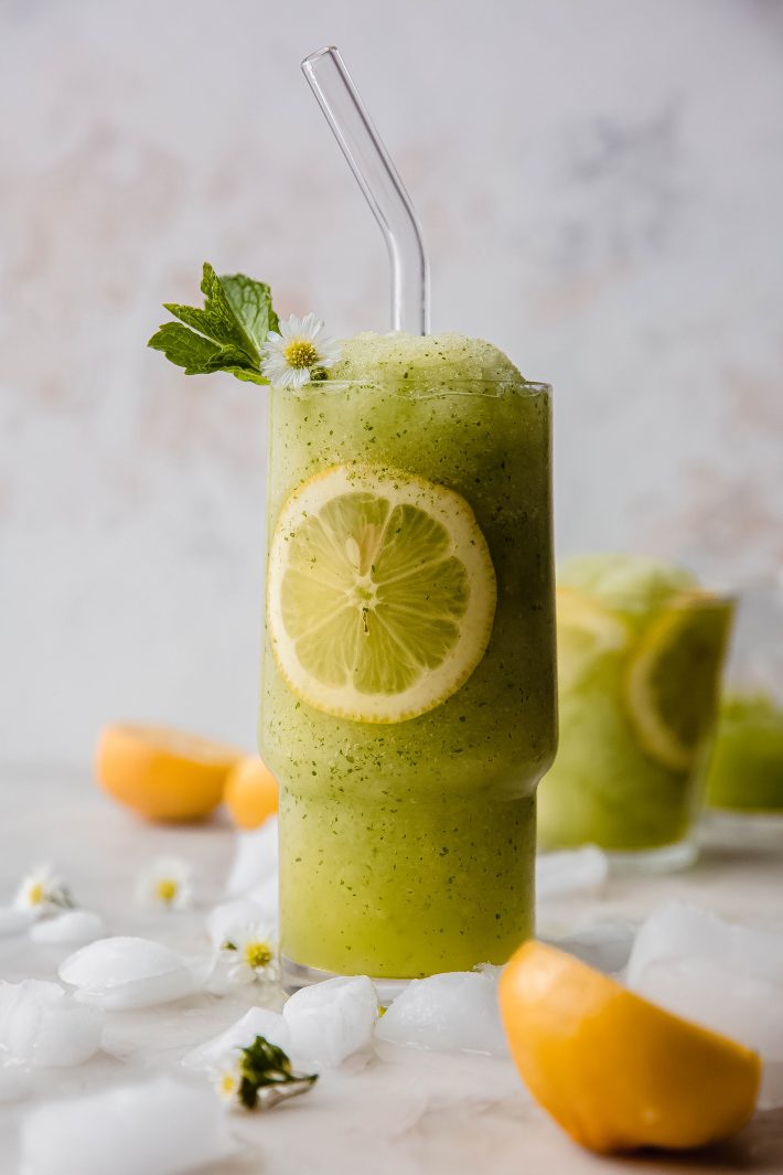 tall glass with frozen mint lemonade, glass straw and lemon slice in glass