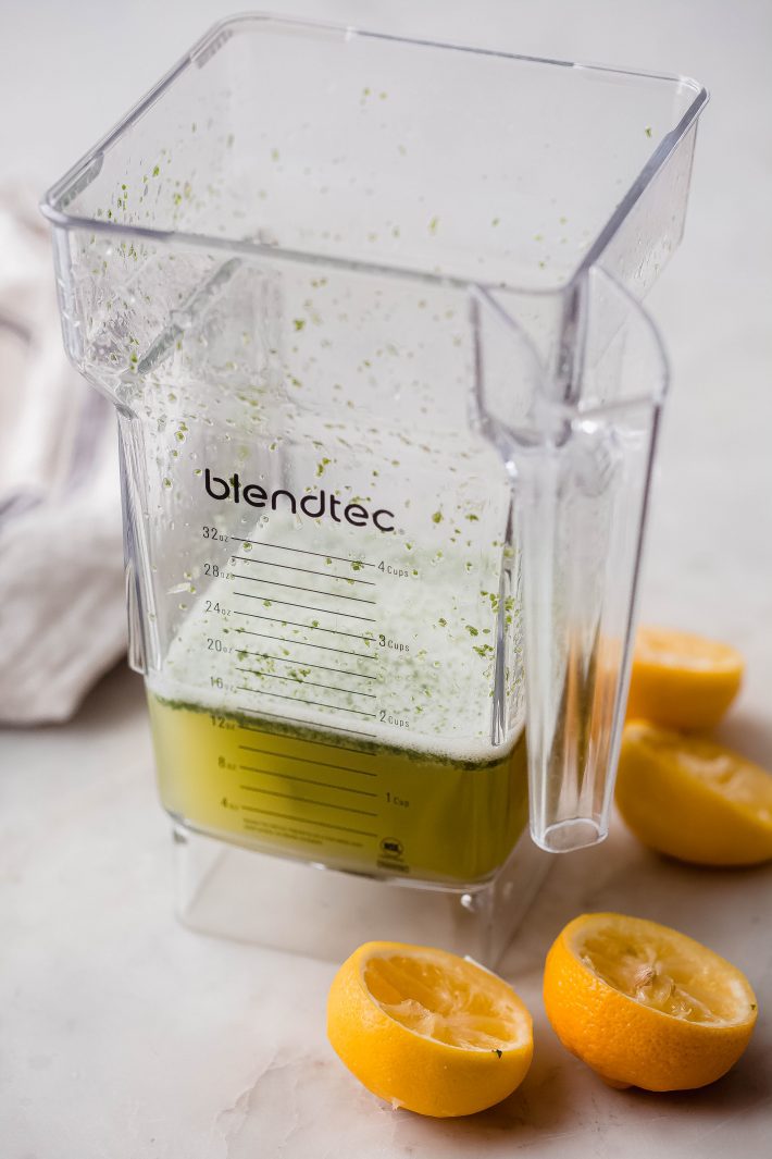 blender with blended lemon juice, lime juice, mint, sugar, and water on white marble