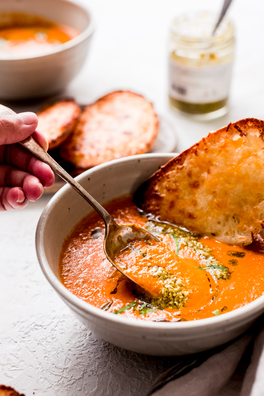 bowl of tomato basil soup with spoon being lifted by hand